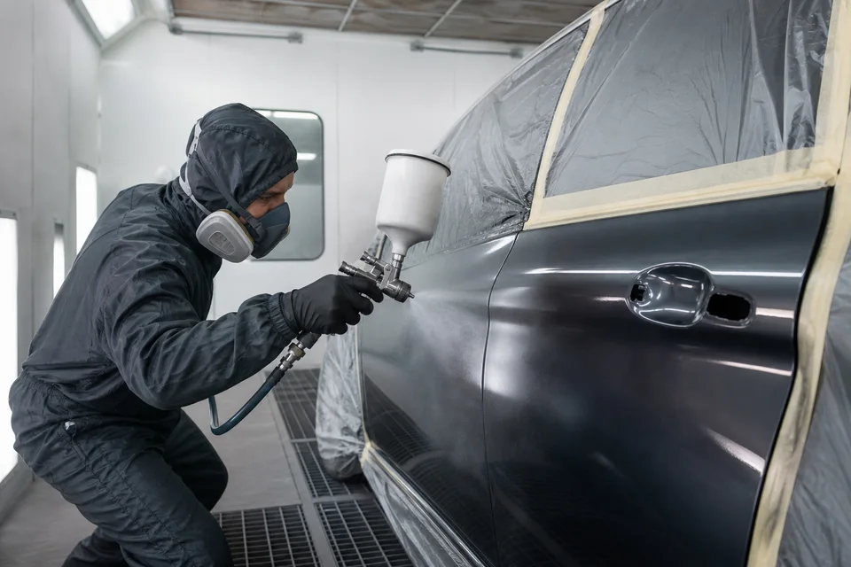 Specialistas dažo automobilio kėbulo detalę apšviestoje dažymo kameroje